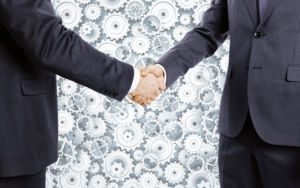 Businessmen shake hands at cogwheels background