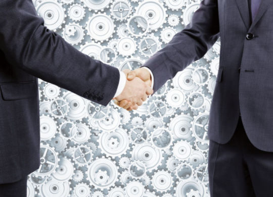 Businessmen shake hands at cogwheels background